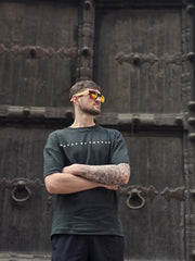 House of SwaSha hunter green oversized men’s t-shirt front view on model, round neck half sleeves, 210 GSM organic cotton standing in front of a large wooden door